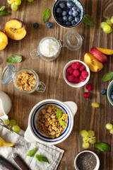 Ingredients for cooking a healthy breakfast setup with granola, assorted fresh fruits, chia seeds and yogurt on a rustic wooden surface top view