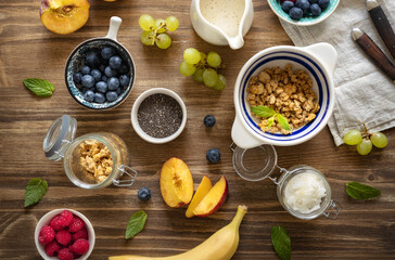 Set of various ingredients for cooking a healthy breakfast setup with granola, assorted fresh fruits, chia seeds and yogurt on a rustic wooden surface top view