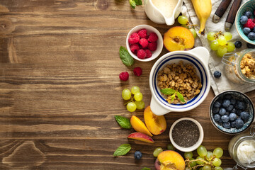 Top view of a healthy breakfast preparation with granola, fresh fruits, chia seeds, and yogurt on a wooden table with copy space