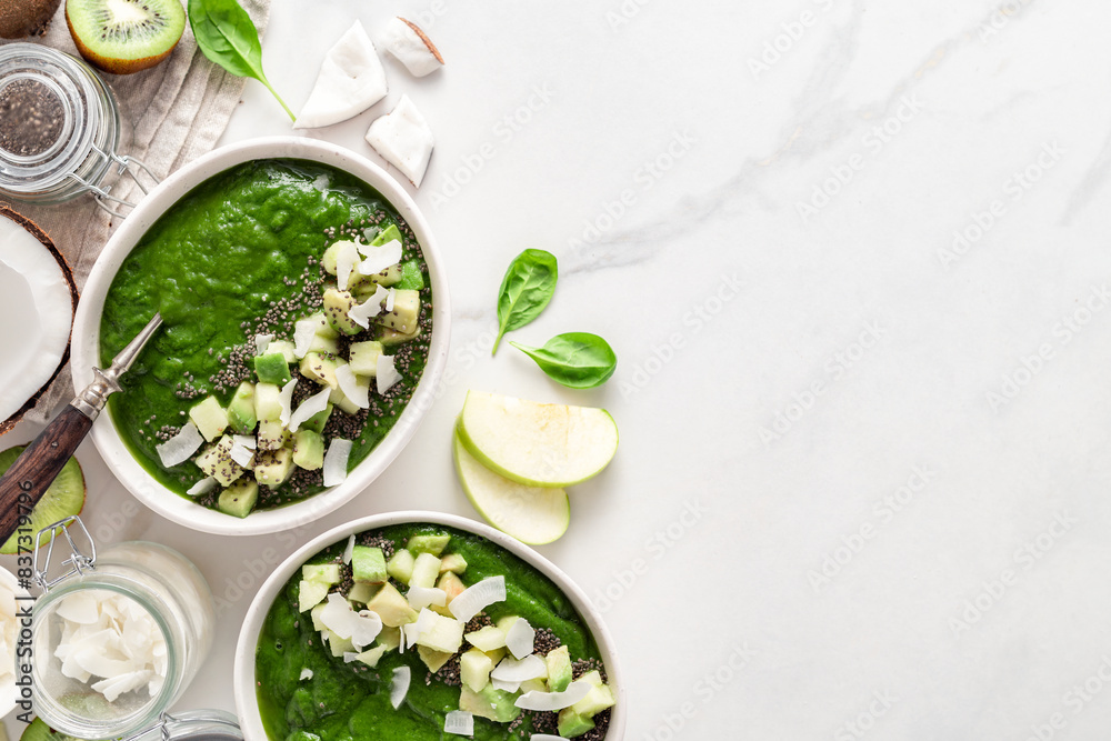 Wall mural Healthy green smoothie bowls topped with avocado, kiwi, apple, coconut milk, spinach and chia seeds. Fresh, vegan, and nutrient-rich breakfast option. Top view on a marble background with copy space