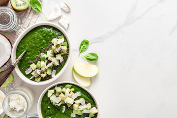 Healthy green smoothie bowls topped with avocado, kiwi, apple, coconut milk, spinach and chia seeds. Fresh, vegan, and nutrient-rich breakfast option. Top view on a marble background with copy space