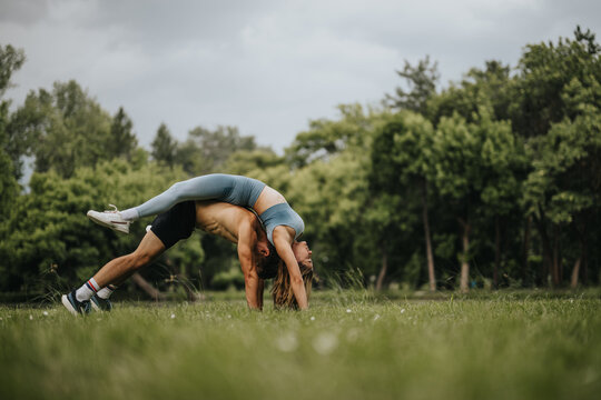 A couple practicing acro yoga in a lush green park, portraying fitness, balance, and trust against a natural backdrop.