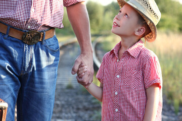 hands of parent and son in cowboy hat near the railroad