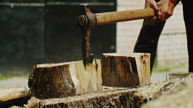 Person chopping wood with an axe on a tree stump, with sawdust flying. Firewood preparation and woodworking concept. Design for poster, banner, and header. Outdoor scene.
