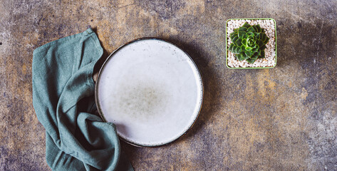 Ceramic empty plate, napkin and potted succulent on textured gray background top view web banner