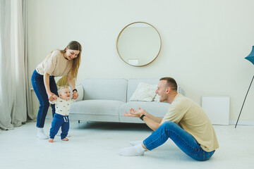 A young married couple is having fun playing with a small child in a modern living room together....