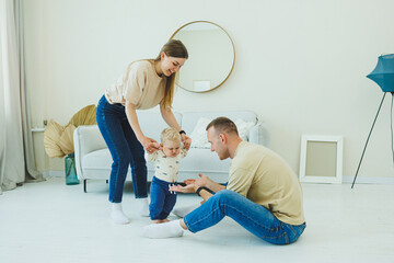 A young married couple is having fun playing with a small child in a modern living room together....