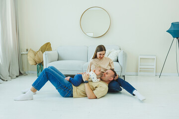 A young married couple is having fun playing with a small child in a modern living room together....