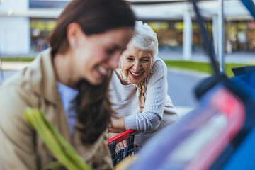 A smiling Caucasian woman and her senior mother load shopping bags into the car trunk,...