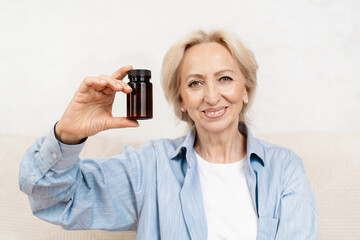 Smiling Senior Woman Holding Medicine Bottle in Her Hand And Sitting On Sofa