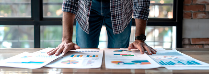 professional man stands at office desk analyzing financial charts on papers,suitable for business training programs,financial analysis workshops,corporate coaching sessions,strategic planning material