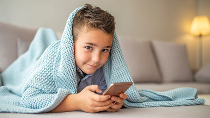 Adorable boy sitting on the sofa in the living room and playing with smartphone. Portrait of a cute...