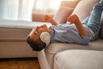 The young boy is smiling and listening to music. Loud music. Cute little relaxed boy listening to the music in big white headphones. Cute little boy with headphones