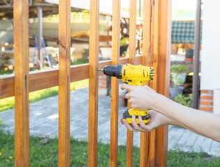 A person is using a drill to attach a wooden fence. The individual is focused on securing the fence...