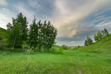 A picturesque scene of rolling green hills, lush meadows, and a distant river, bathed in the soft glow of a spring afternoon.
