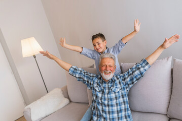 Laughing grandfather with his grandson as they play together indoors in the living room with the...