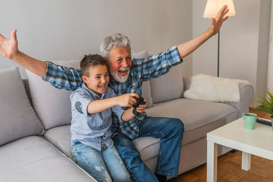 Grandfather and grandson playing video game with console, happy time together. Grandfather with his nephew seated on a sofa playing video games. Grandfather and child playing game console