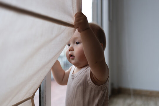 A curious baby pulls the curtain aside, discovering the world beyond the window with wonder