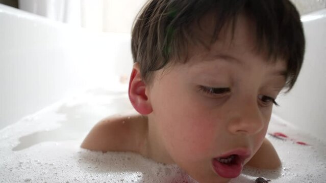 Young boy lying in the bathtub filled with bubbles, looking down at his toy. The moment is peaceful and highlights the simple joys and relaxation found in everyday bath time routines