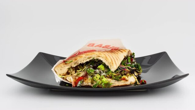 Rotting d&ouml;ner kebab sandwich timelapse isolated on white. The doner is lying on a plate and getting moldy. Composting meal in a studio environment with vegetables and salad.