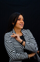 chica latina sonriendo con fondo negro usando una blusa negra y una chaqueta de rayas blanca y negra