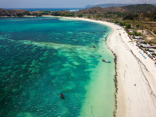 Aerial view of a quiet tropical beach with wooden shacks and warm, shallow ocean