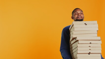 Confident male courier carrying big pile of pizza boxes to deliver fast food order to clients,...