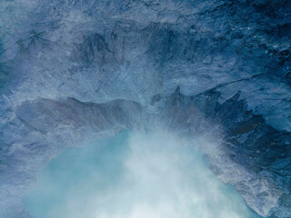 Top view of Ijen rocky mountain volcano with a crater hole in the middle, surrounded by grey clouds...