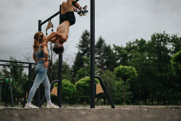 Man and woman performing outdoor calisthenics workout at a park fitness station, showing teamwork...