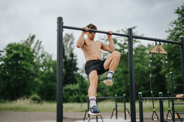 Young man performing pull-ups on metal parallel bars in an outdoor gym, focusing on fitness and strength training.