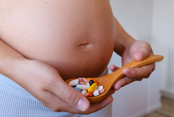 Unrecognazied Pregnant Woman With Belly Holding Wooden Spoon With Prenatal Vitamins. Pregnancy Supplements Pills. Closeup.