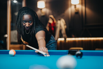 Focused young woman playing pool at a bar, having a joyful night out with friends, expressing...