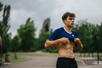 Young athlete in a blue shirt showing off his toned abs during an outdoor workout session. The...