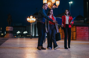 Young professionals engaged in an outdoor business meeting at night, discussing a project under...