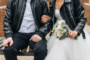 young caucasian couple in black leather jackets sit on bench, bride and groom, cropped, unrecognizable, no face