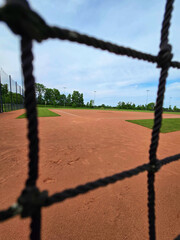 A baseball field shot through protective netting on a sunny day.