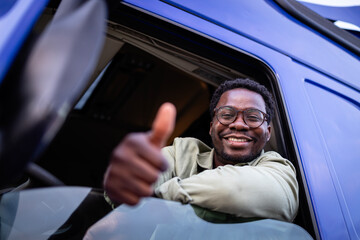 Professional driver sitting in his truck and holding thumbs up.