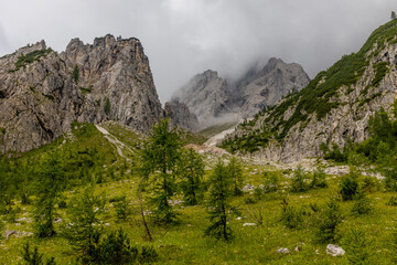 Obraz premium Dolomiti Alps beautiful mountain landscape. Rocky tower alpine summits in the Dolomites. Summer mountain scenic view on the hiking trekking path in the green mountain valley and blue sky with clouds