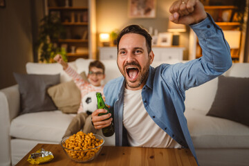 Father and son with football ball watch football match cheer at home
