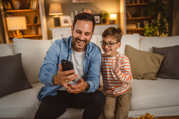 Father and son use mobile phone for video call at home