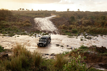 Safari vehicle crossing rushing river during rain storm