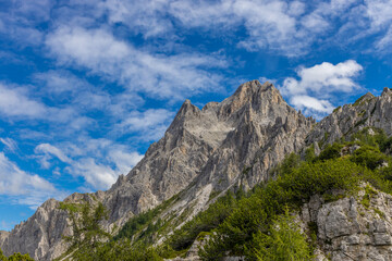 Fototapeta premium Dolomiti Alps beautiful mountain landscape. Rocky tower alpine summits in the Dolomites. Summer mountain scenic view on the hiking trekking path in the green mountain valley and blue sky with clouds