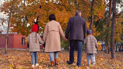 Happy kids holding hands with mom dad, walking through autumn park. Son, Daughter Mom Dad Walking...