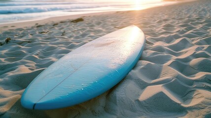 Blue surfboard on sandy beach at sunset with ocean in background