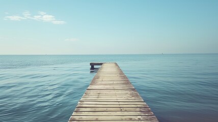 Fototapeta premium Wooden pier extends into calm, blue ocean under clear sky