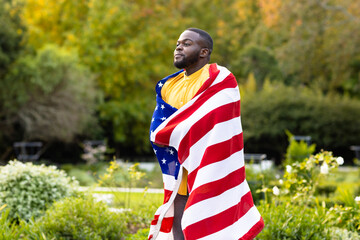 Happy african american man covered with flag of usa in garden