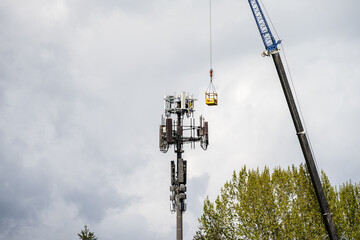 Mobile cell site tower antenna and top electronics repair and maintenance, crane with personnel bucket attached and raised up to antenna level, telecommunications industry background
