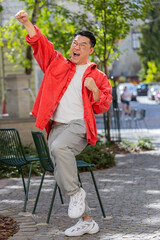 Asian middle-aged man shouting celebrating success winning goal achievement good news lottery jackpot casino luck victory career outdoors. Chinese guy on urban city street. Town lifestyles. Vertical
