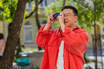 Asian middle-aged man tourist traveling on weekends exploring town, making photo pictures on retro vintage camera outdoors. Chinese mature guy on urban city street. Horizontal. Lifestyles