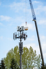 Mobile cell site tower antenna and top electronics repair and maintenance, crane with personnel bucket attached and raised up to antenna level, telecommunications industry background
